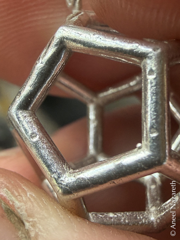 Small divots on the silver surfaces of a dodecahedron left over from the 3D Printing sprues